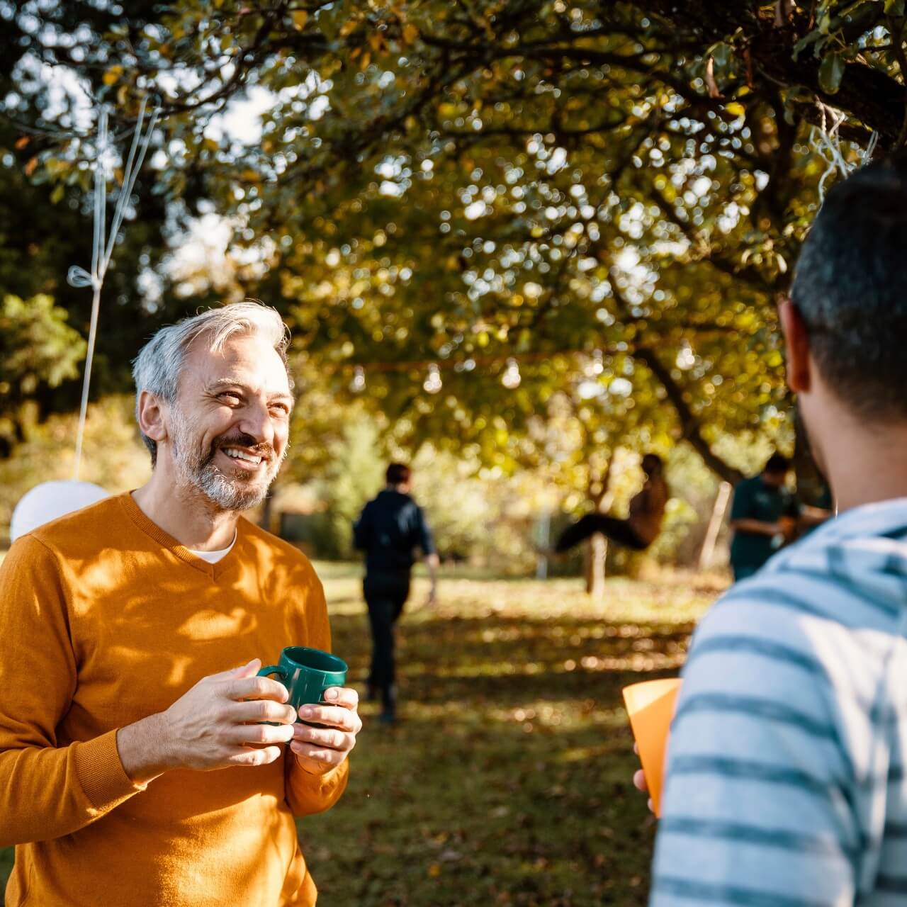 Man in a orange tshirt smiling in a park talking to his friends