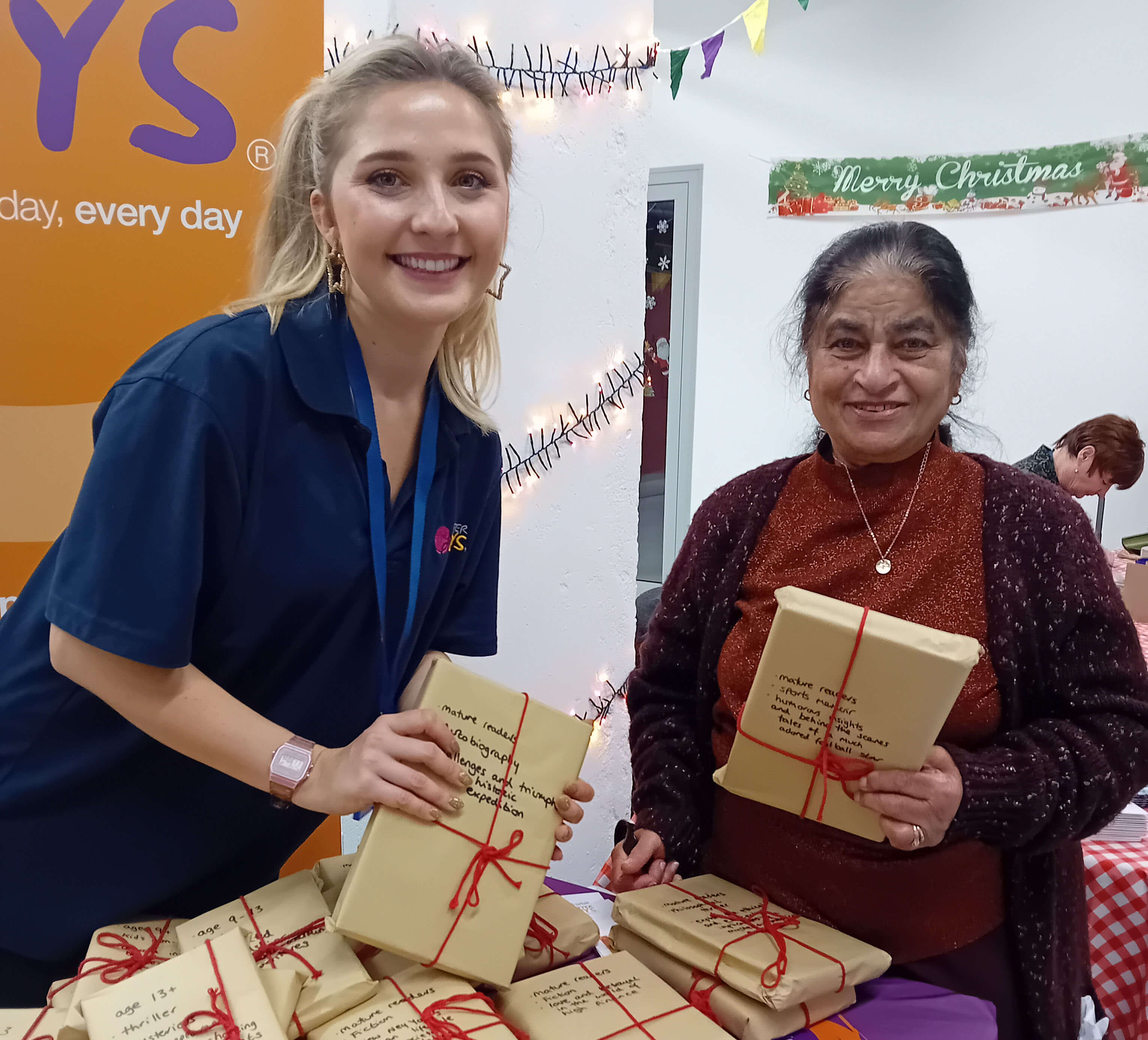 Two ladies holding wrapped gifts in brown paper and smiling