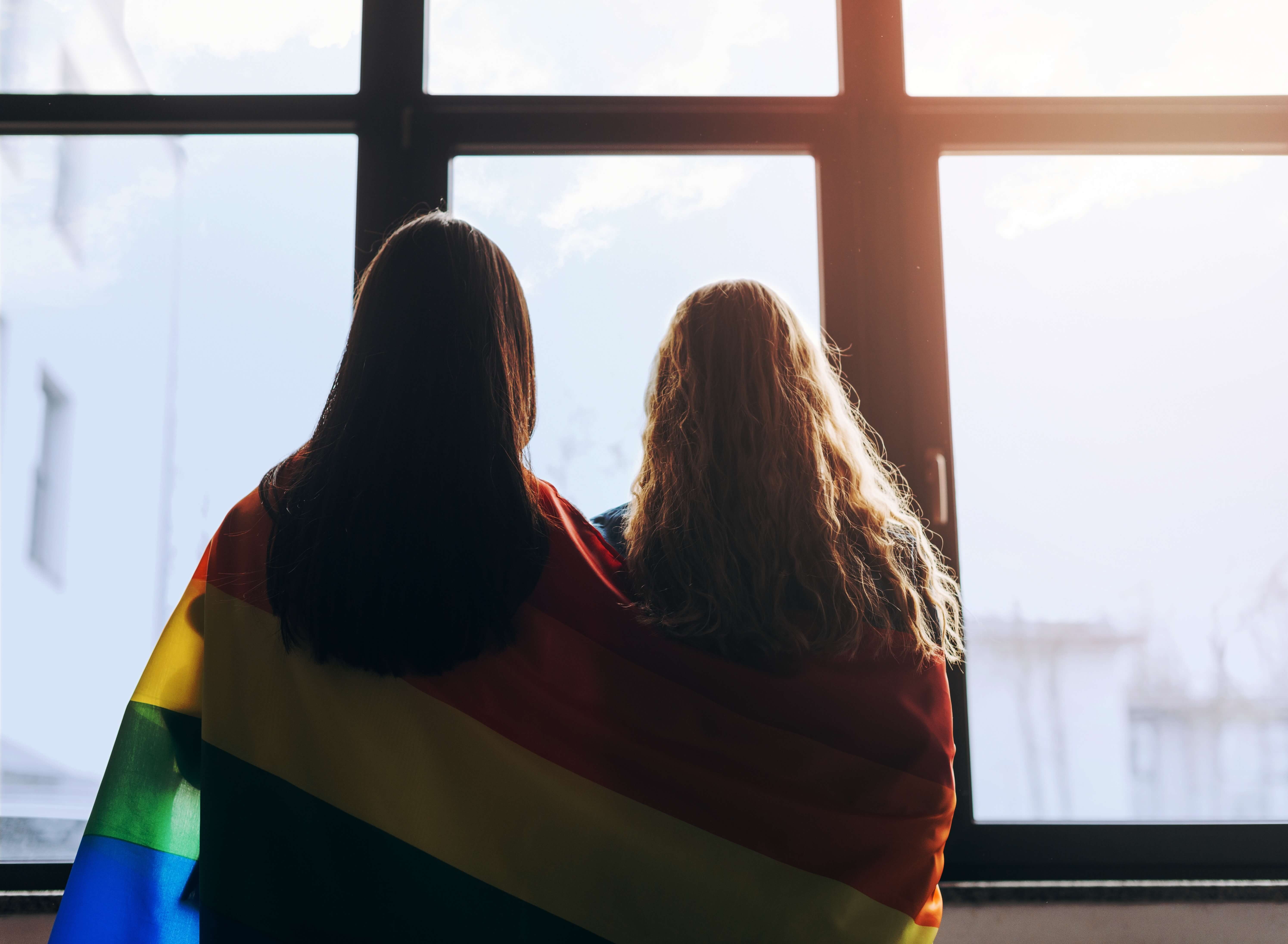 Two women wearing a LGBTQ+ flag around their shoulders