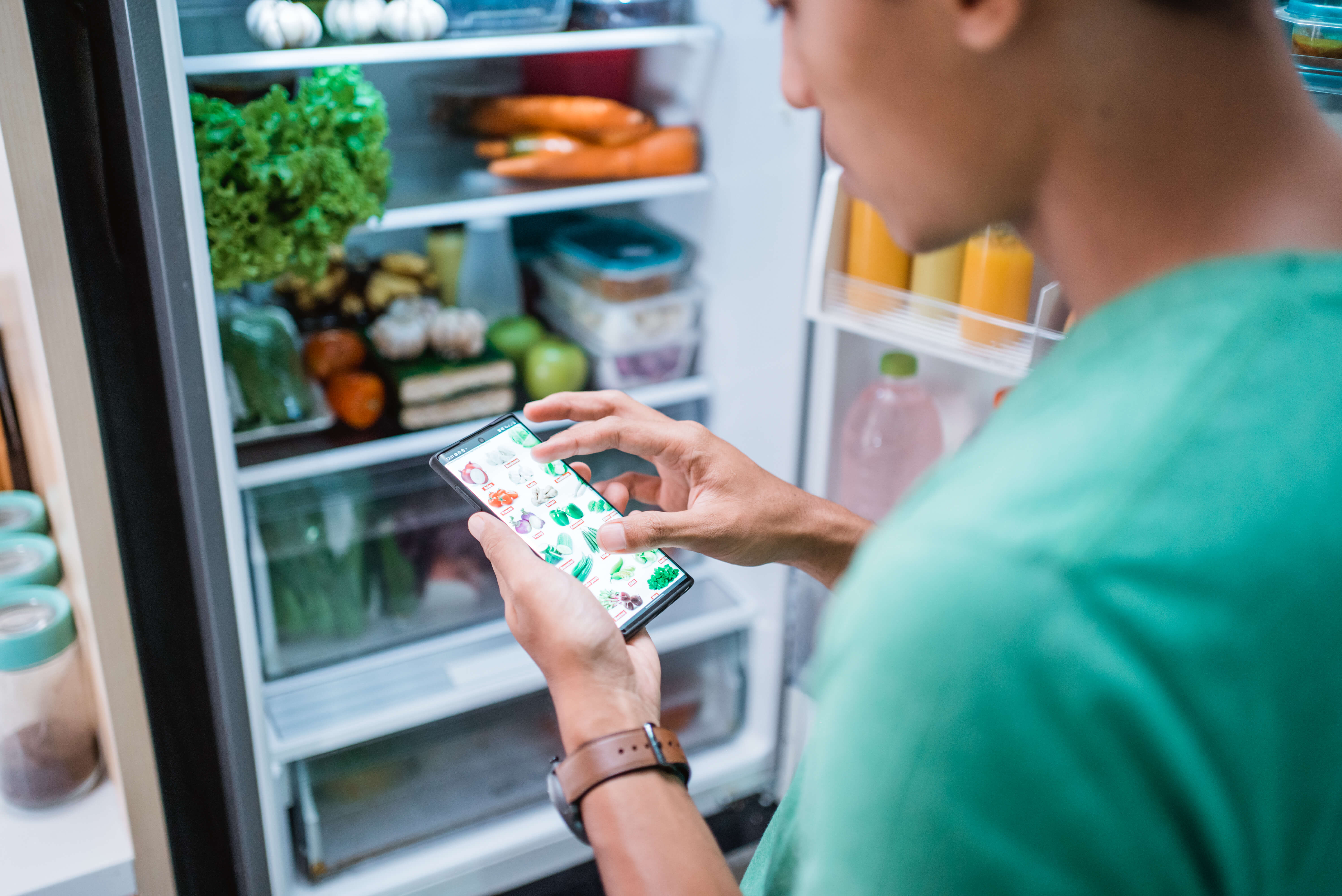 person looking in fridge at groceries checking what to purchase on a mobile app